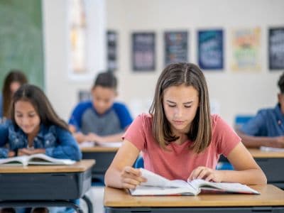 Student reading a textbook in a classroom, representing the learning challenges and academic support needs of neurodivergent students and children with learning disabilities.